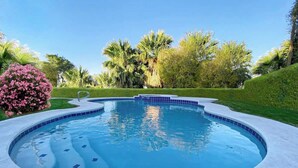 A swimming pool with a curved edge, surrounded by a concrete deck and lush greenery. - LUX 7BR/4BA Villa w/Heated Pool, next to the Strip (Las Vegas)