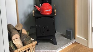 A compact wood-burning stove with a chimney, a red pot on top, and a basket of firewood.