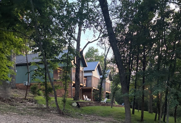 Une cabane au revêtement extérieur en bois, entourée d’arbres et bordée d’une zone herbeuse.