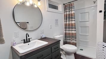 A modern bathroom with a round mirror, a white sink, dark wooden cabinets, a white toilet, and a shower with a plaid curtain.