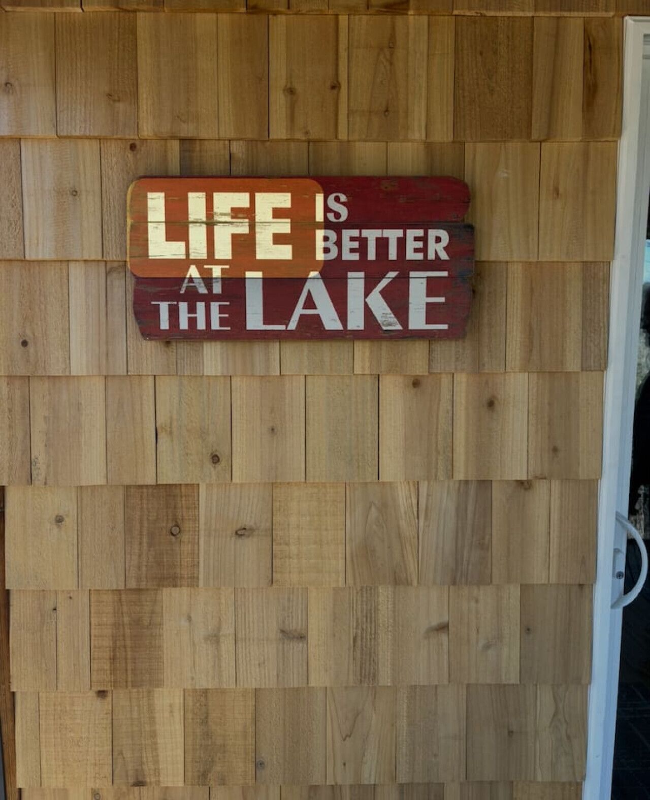 Een houten wand met een bord waarop staat: LIFE IS BETTER AT THE LAKE.