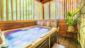 A hot tub in a wooden cabin with a stone wall and a plant on a small table.