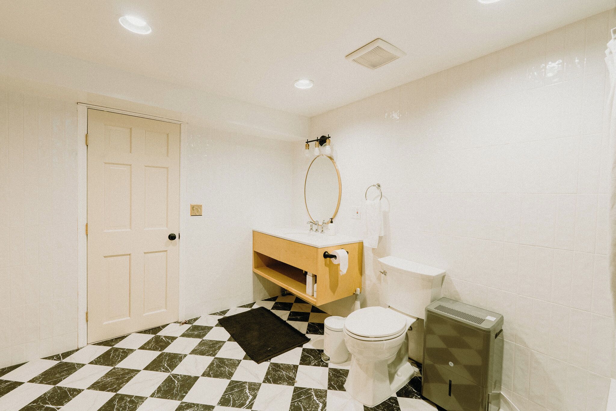 A bathroom with a checkered floor, a toilet, a sink with a mirror, and a door.