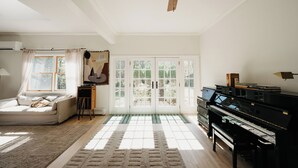 A living room with a piano, a sofa, a ceiling fan, and a view through glass doors to the outside. - Group Getaway: Sleeps 15, 11 Priv Acres, Wood fire hot tub, sauna, karaoke (Margaretville)