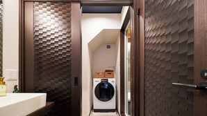 Un pasillo estrecho con una lavadora y cestas en un estante, paredes de madera texturizada y un lavabo blanco.