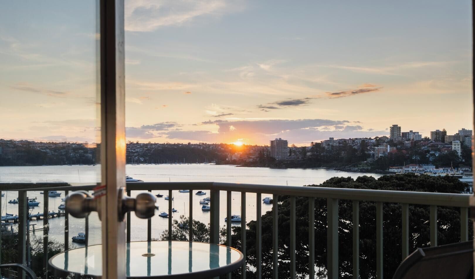 A balcony with a view of a sunset over a body of water, boats, and a cityscape.