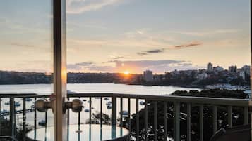 A balcony with a view of a sunset over a body of water, boats, and a cityscape.