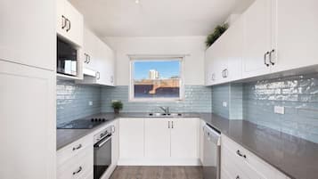 Una cocina moderna con armarios blancos, un lavamanos de acero inoxidable y una ventana con vistas a edificios.