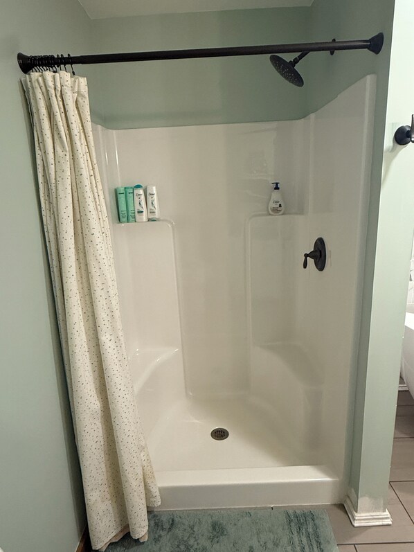 Une douche avec une porte en verre transparent, un pommeau de douche et un rideau.