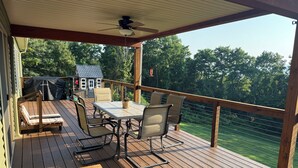 Une terrasse en bois avec une table et des chaises, un barbecue abrité et une vue sur une maison et des arbres.