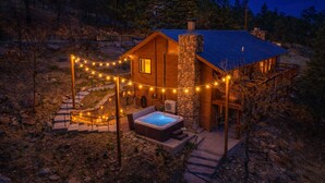 A cabin with a stone chimney, a hot tub, and string lights. - Beautiful log cabin high above the Rio Ruidoso River. The Log & Order Cabin. (Ruidoso)
