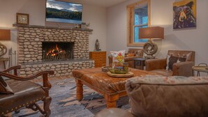 A living room with a stone fireplace, leather furniture, a television, and a painting on the wall. - Beautiful log cabin high above the Rio Ruidoso River. The Log & Order Cabin. (Ruidoso)