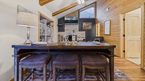 A rustic kitchen with a wooden ceiling, a bar area with stools, a fireplace, and a large window overlooking a lake. - Beautiful log cabin high above the Rio Ruidoso River. The Log & Order Cabin. (Ruidoso)