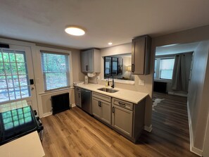 A modern kitchen with a central island, built-in appliances, and a view of the backyard through the windows. - Charming First Floor 1-Bedroom - Steps Unionville Center Shops (Farmington)