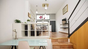 Un salon moderne avec un bureau en verre, un canapé blanc et un escalier.