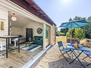 Eine überdachte Terrasse mit Esstisch, Stühlen und einem blauen Sonnenschirm.