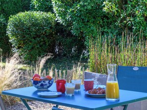Ein Tisch draußen gedeckt mit verschiedenen Frühstücksartikeln, darunter Obst, eine Schüssel, eine rote Tasse und ein Krug Saft.
