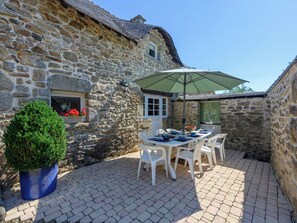 A stone building with a patio area featuring a table and chairs, a potted plant, and a window with flowers.