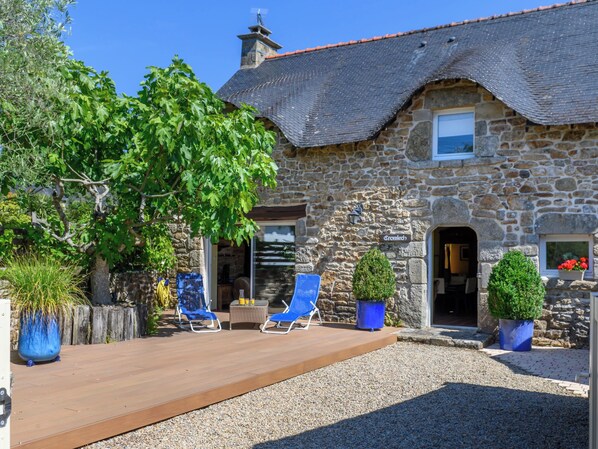 A stone building with a thatched roof, a wooden deck, and two blue lounge chairs.