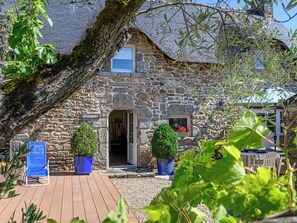 A stone house with a wooden deck, two potted plants, and a chair.