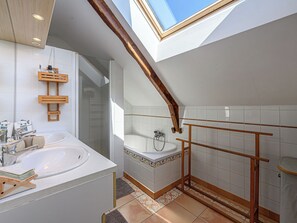 A modern bathroom with a skylight, a large bathtub, and a separate shower area.