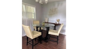 Uma área de refeições com uma mesa redonda de vidro e quatro cadeiras, um candelabro e um objeto decorativo na parede.