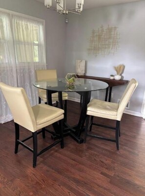 A dining area with a round glass table and four chairs, a chandelier, and a decorative wall piece.