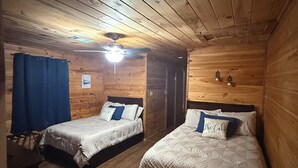 Een kamer in chaletstijl met twee bedden, houten wanden, een plafondventilator en een kleine tafel.
