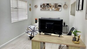 Et moderne soveværelse med en seng, et skrivebord med en computer, et vindue med persienner og et kunstværk på væggen.