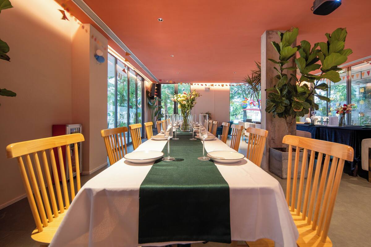 A long dining table with white tablecloths and green runners, flanked by wooden chairs.