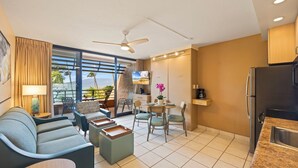 A modern living room with a sofa, coffee table, and dining area. There is a balcony with a view of palm trees and mountains. - Kuleana Club - 509 (Lahaina)