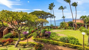 A tropical garden with a pathway, palm trees, and a view of the ocean. - Kuleana Club - 509 (Lahaina)