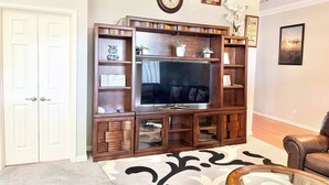 Un salon doté d’un grand téléviseur, d’un meuble de rangement en bois et d’un tapis à motifs.