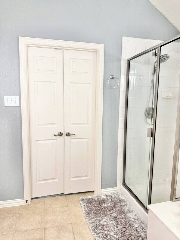 A bathroom with a white door, a glass shower enclosure, and a beige tiled floor.