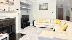 Un salon avec une cheminée, un ensemble de canapés, un téléviseur et une horloge au mur.