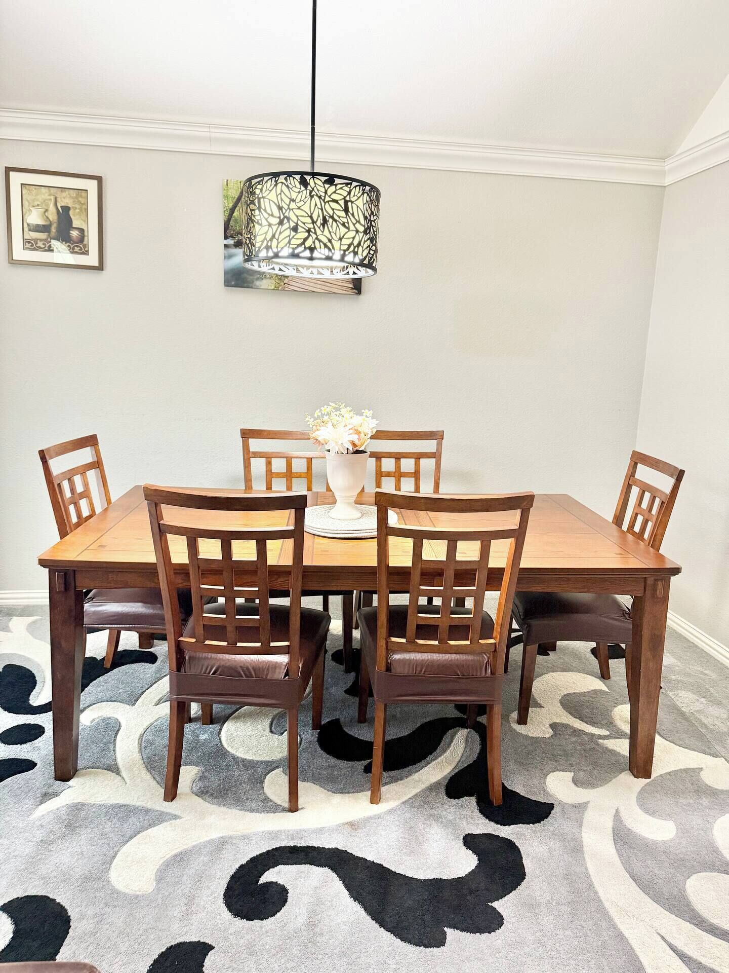 Une salle à manger avec une table et des chaises en bois, un vase rempli de fleurs et un luminaire suspendu.