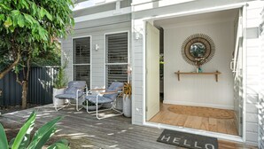 Ein gemütlicher Sitzbereich im Freien mit zwei Stühlen und einem Tisch, einer Holzterrasse und einer weißen Tür mit einer Fußmatte, auf der 'HELLO' steht.