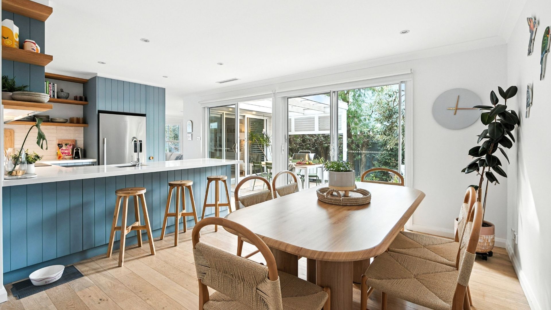 A modern kitchen with blue cabinets, a wooden dining table, and bar stools.