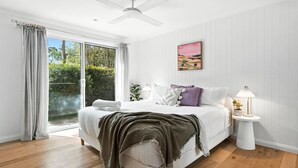 Ein Schlafzimmer mit einem großen Bett, einem Deckenventilator, einem Fenster mit Vorhängen, einem Nachttisch mit einer Lampe und einem Gemälde an der Wand.