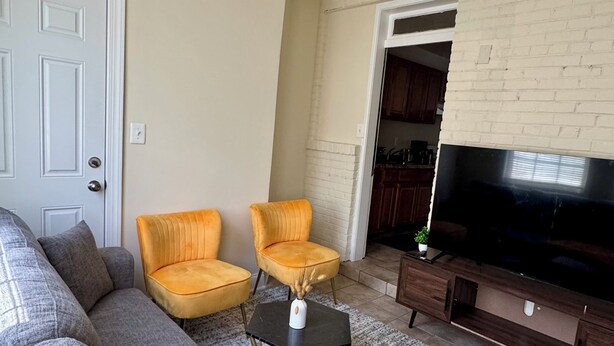 A living room with a grey sectional sofa, two yellow chairs, a small black coffee table, and a flat-screen TV on a wooden stand.