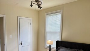 A bedroom with a bed, a nightstand, a ceiling fan, a window with blinds, and a door.