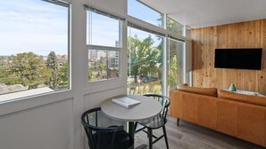 A modern living room with large windows, a round table, a sofa, and a flat-screen TV on the wall. - FREE PARKING, Downtown Views w/ Kitchen + Wi-Fi (Spokane)