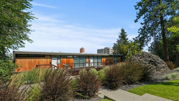 A modern building with a wooden facade, surrounded by a landscaped garden with various shrubs and a large rock formation. - FREE PARKING, Downtown Views w/ Kitchen + Wi-Fi (Spokane)