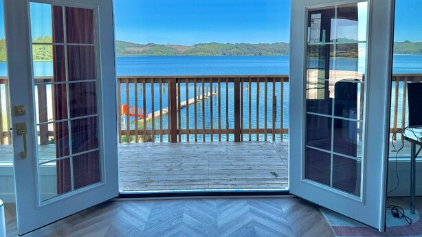 Une porte ouverte donnant sur un balcon d’où l’on peut admirer un lac et des collines lointaines.