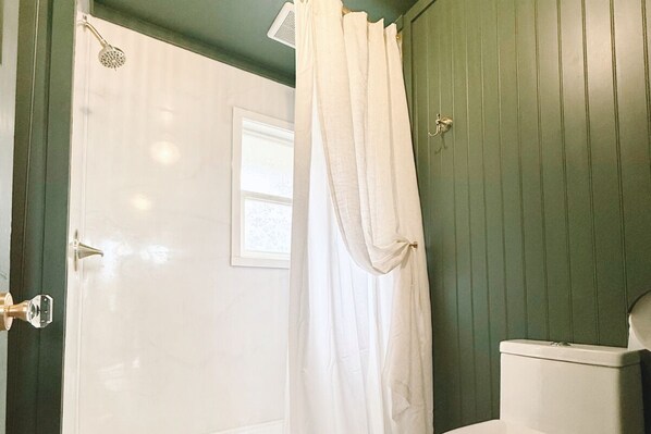 A bathroom with a white shower curtain, a white toilet, and green walls.