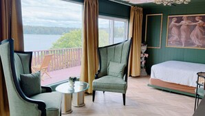 Ein Zimmer mit einem Bett, zwei Sesseln, einem kleinen Tisch und Seeblick durch große Fenster.