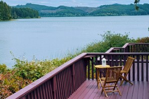 Een houten terras met een tafel en stoelen, met uitzicht op een meer.