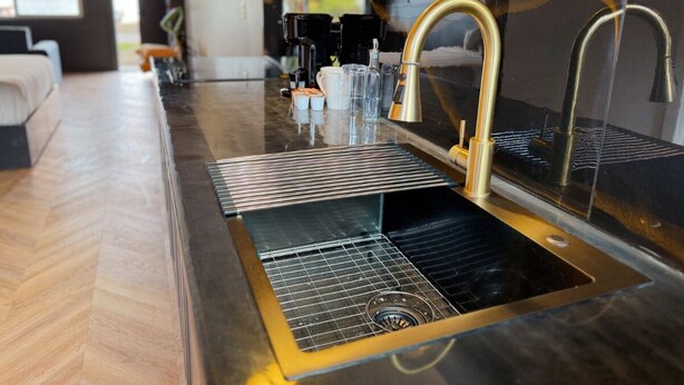 A modern kitchen with a stainless steel sink, gold faucets, and a black countertop. - Lakeside Studio w/ Fishing, boat ramp, dock, kayak (Dunes City)