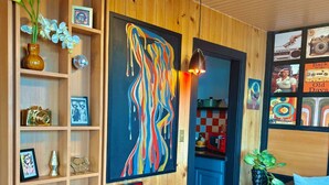 Ett rum med träpanel på väggarna, en stor abstrakt målning, en discokula och olika inramade bilder och föremål på hyllor.