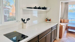 Une cuisine moderne dotée d’une plaque de cuisson à induction noire, de meubles blancs et d’une fenêtre donnant sur un paysage pittoresque.